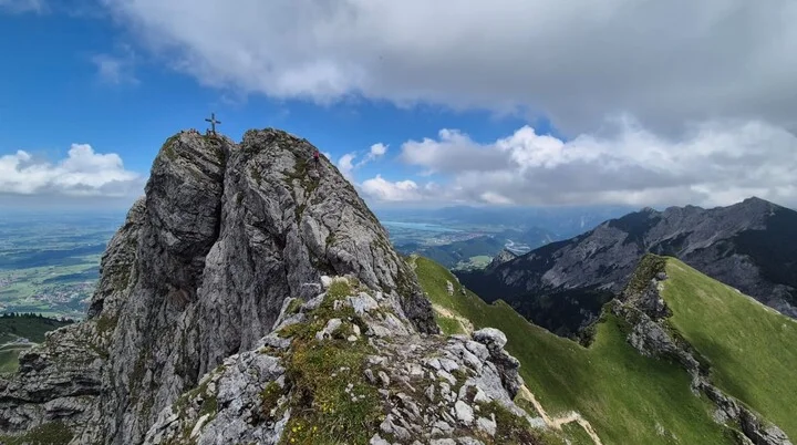 Aggenstein 10 | © DAV-FN / Karin B., Silke S., Robert H. Felsgipfel mit Gipfelkreuz am Aggenstein, umgeben von grünen Bergwiesen und bewölktem Himmel | © DAV-FN / Karin B., Silke S., Robert H.