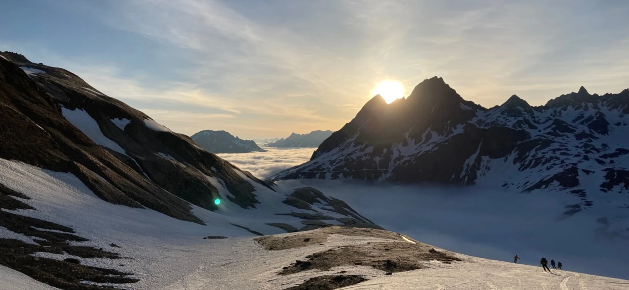 Abfahrt bei der Tour de Soleil | © DAV-FN / P. Schäfer Abfahrende Skifahrer in ein nebelverhangenes Tal gegen die untergehenden Sonne | © DAV-FN / P. Schäfer